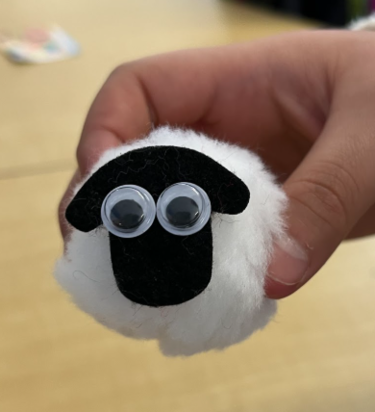 A white pom pom with a black piece of cardboard for a face.