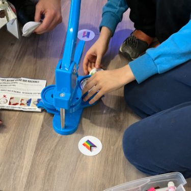 Students using a blue machine to make Pride flag buttons.